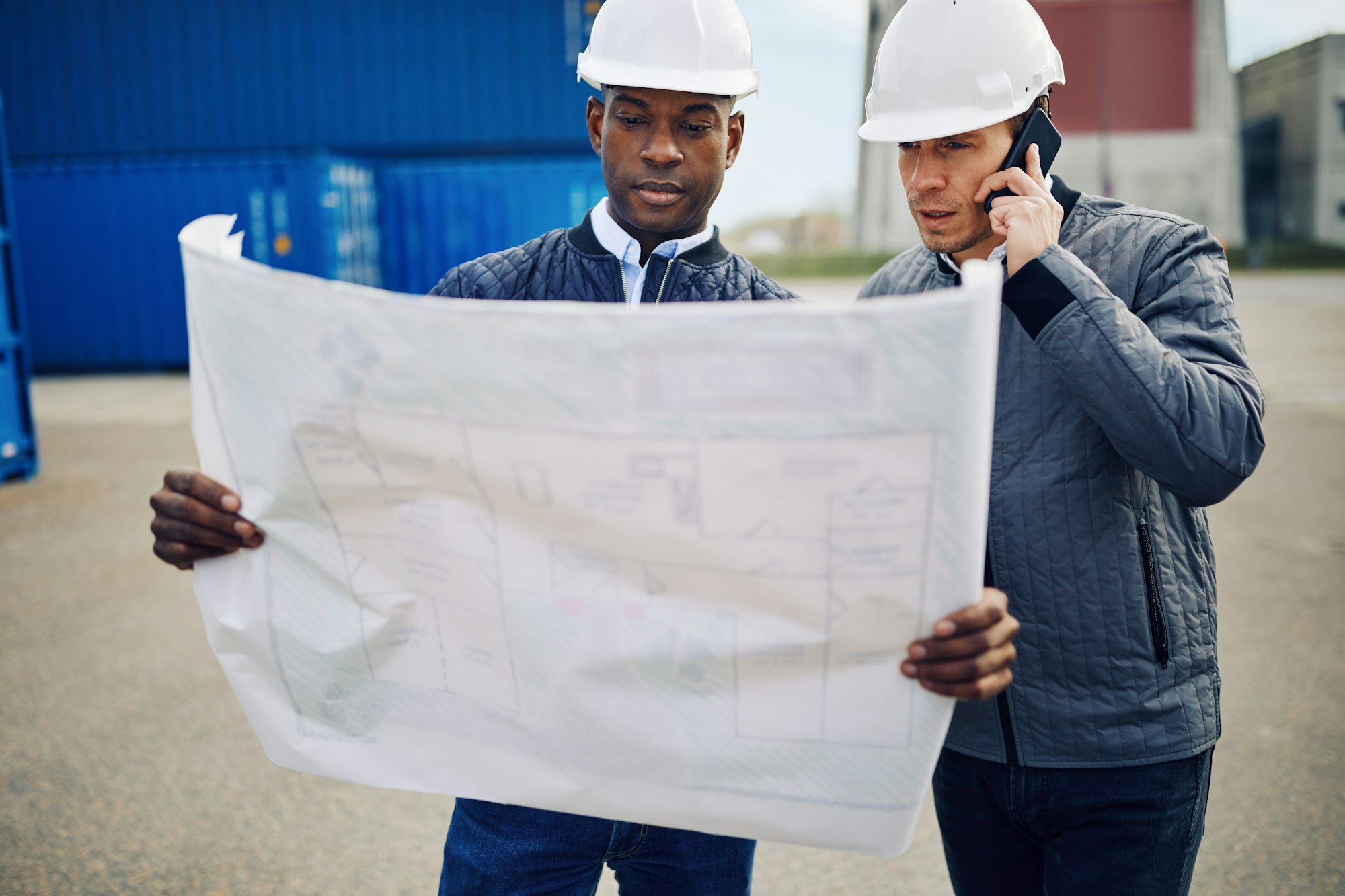 Engineers discussing building plans while standing in a shipping yard